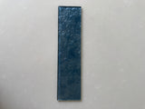 Roca Lux Indigo 3x12 glass tile, natural stone finish with blue and indigo hues, close-up of textured surface.