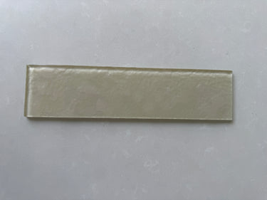 Close-up of Roca Lux Champagne 3x12 natural stone glass tile showing its textured, shimmering champagne-colored surface.
